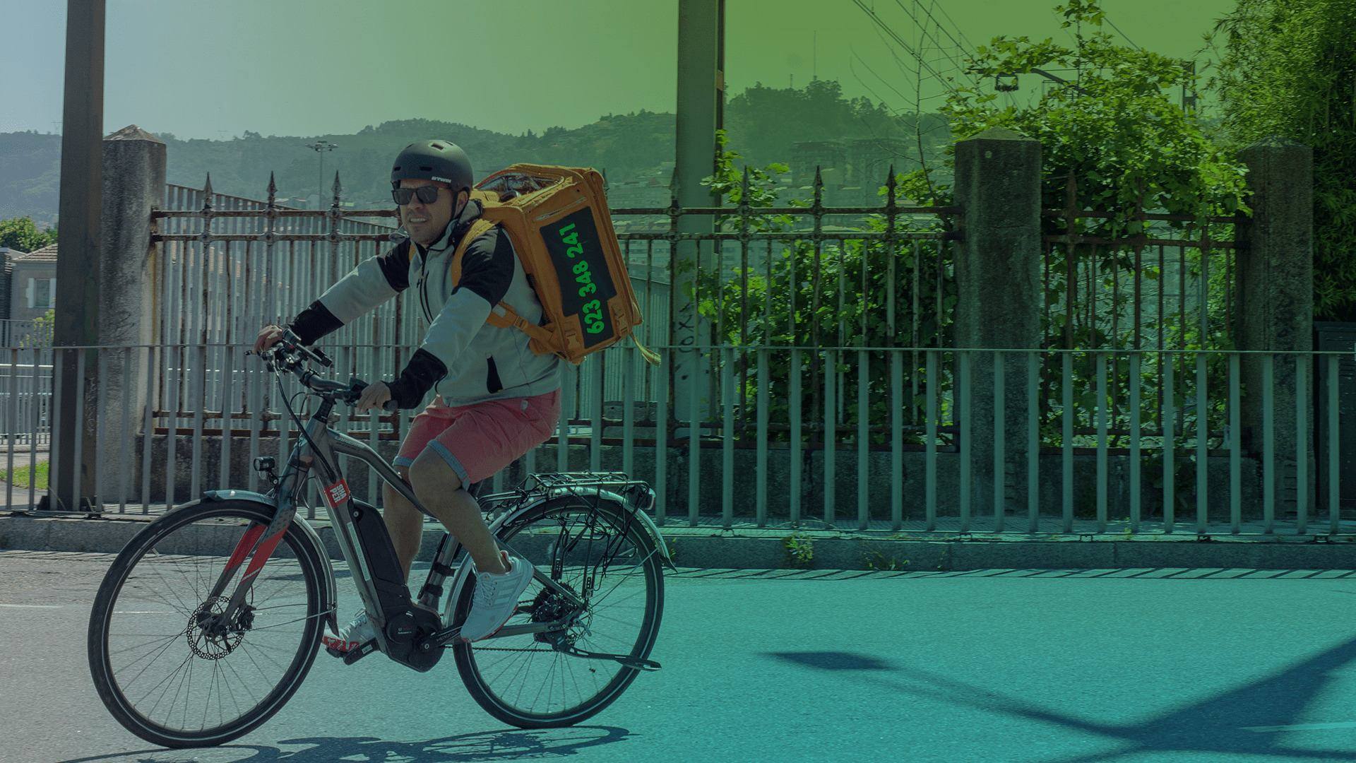 Rider de HomeDelivery en bicicleta eléctrica con la mochila naranja junto al paseo de Vigo