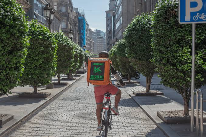 Rider de HomeDelivery pedaleando por una calle arbolada de Vigo